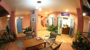 A lobby with a wooden reception desk, several chairs, potted plants, and a staircase leading to an upper level. - Le Bar Tarry Hotel (Tha Li)