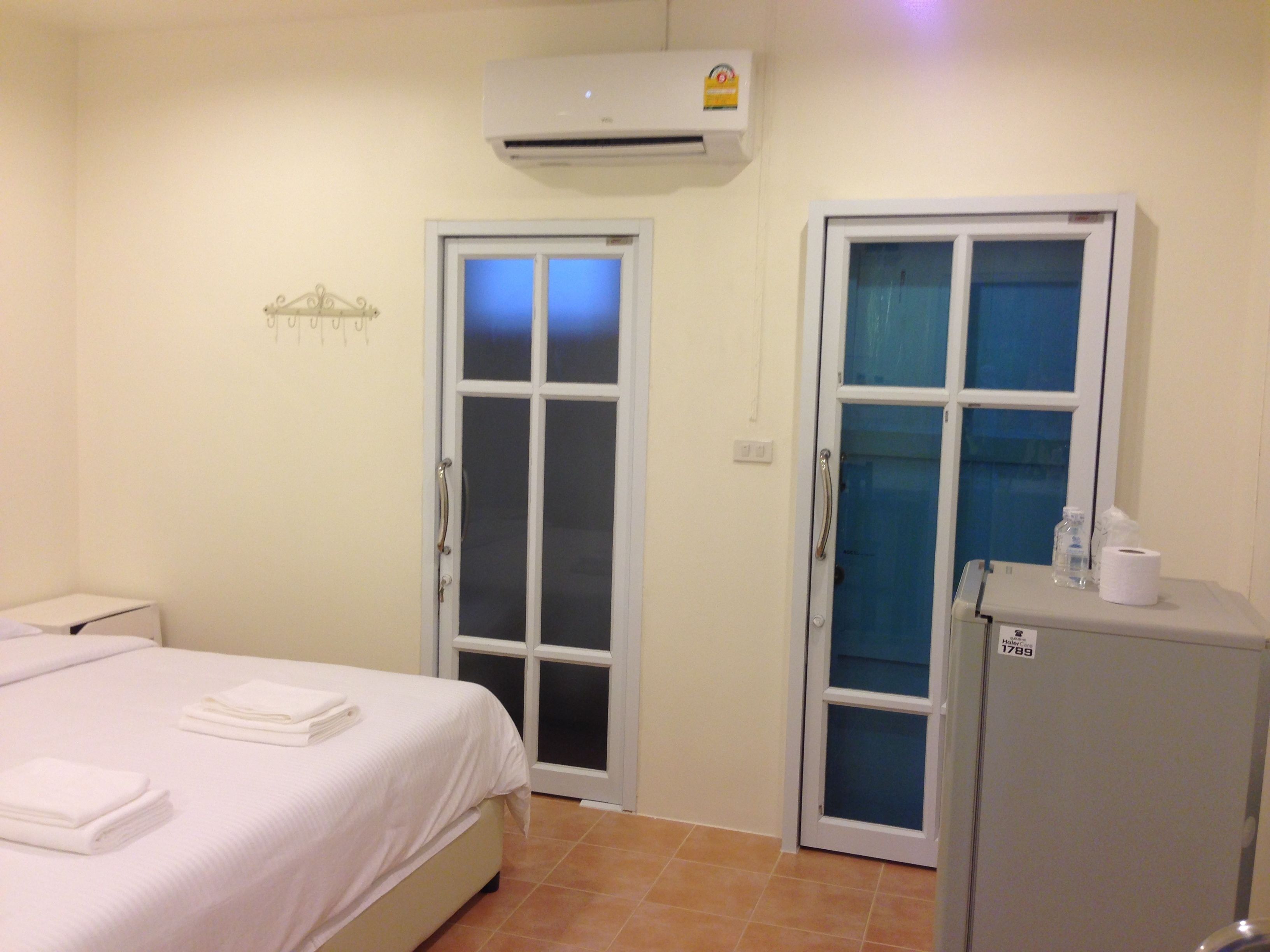 A hotel room with a bed, a small table with toiletries, an air conditioner, and two doors.