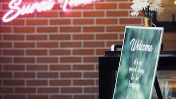 A brick wall with a neon sign and a welcome sign with a beverage image.