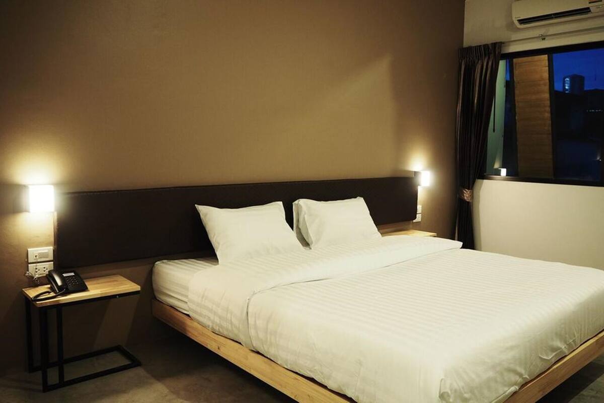A hotel room with a bed, bedside lamps, a telephone, and an air conditioning unit.