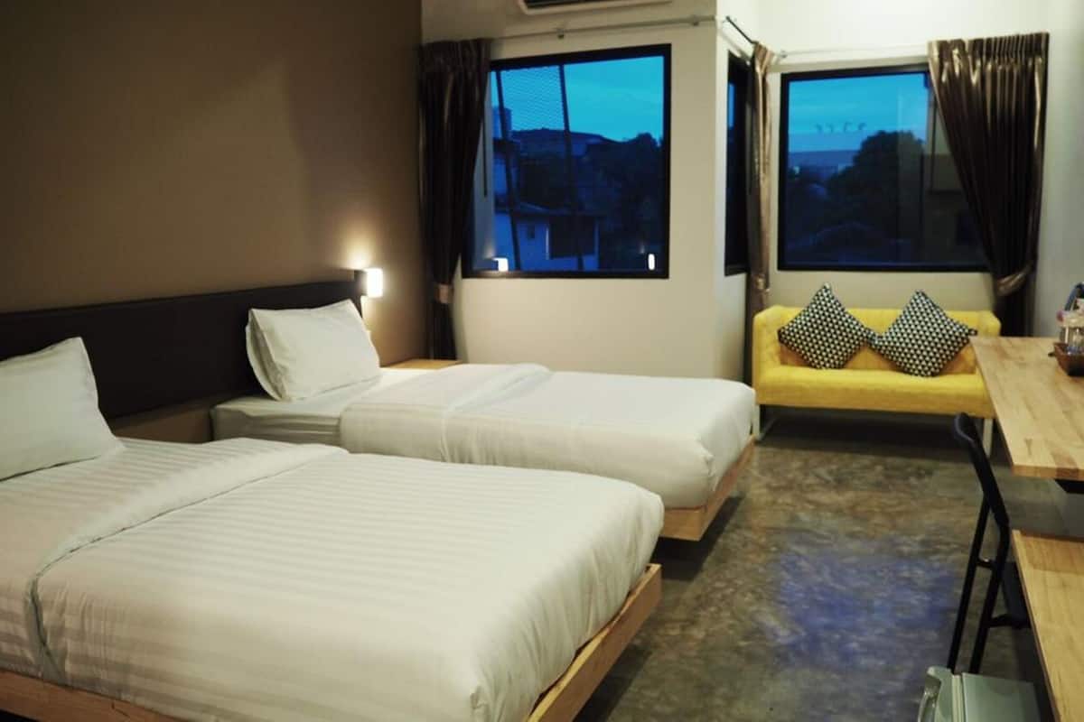 A hotel room with two beds, a sofa with patterned cushions, and a view of the cityscape through the windows.