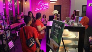 Un espacio interior bien iluminado con un letrero de neón que dice "A3 Living Surat Thani" y un cartel de bienvenida con un mensaje sobre la felicidad.