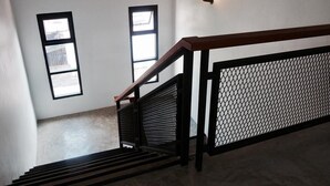 Una escalera con barandilla de madera y protectores de malla metálica, que conduce a un rellano con dos ventanas.