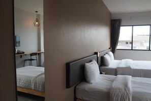 A hotel room with two beds, a large mirror, a desk, and a view of buildings outside. - A3 Living (Surat Thani)