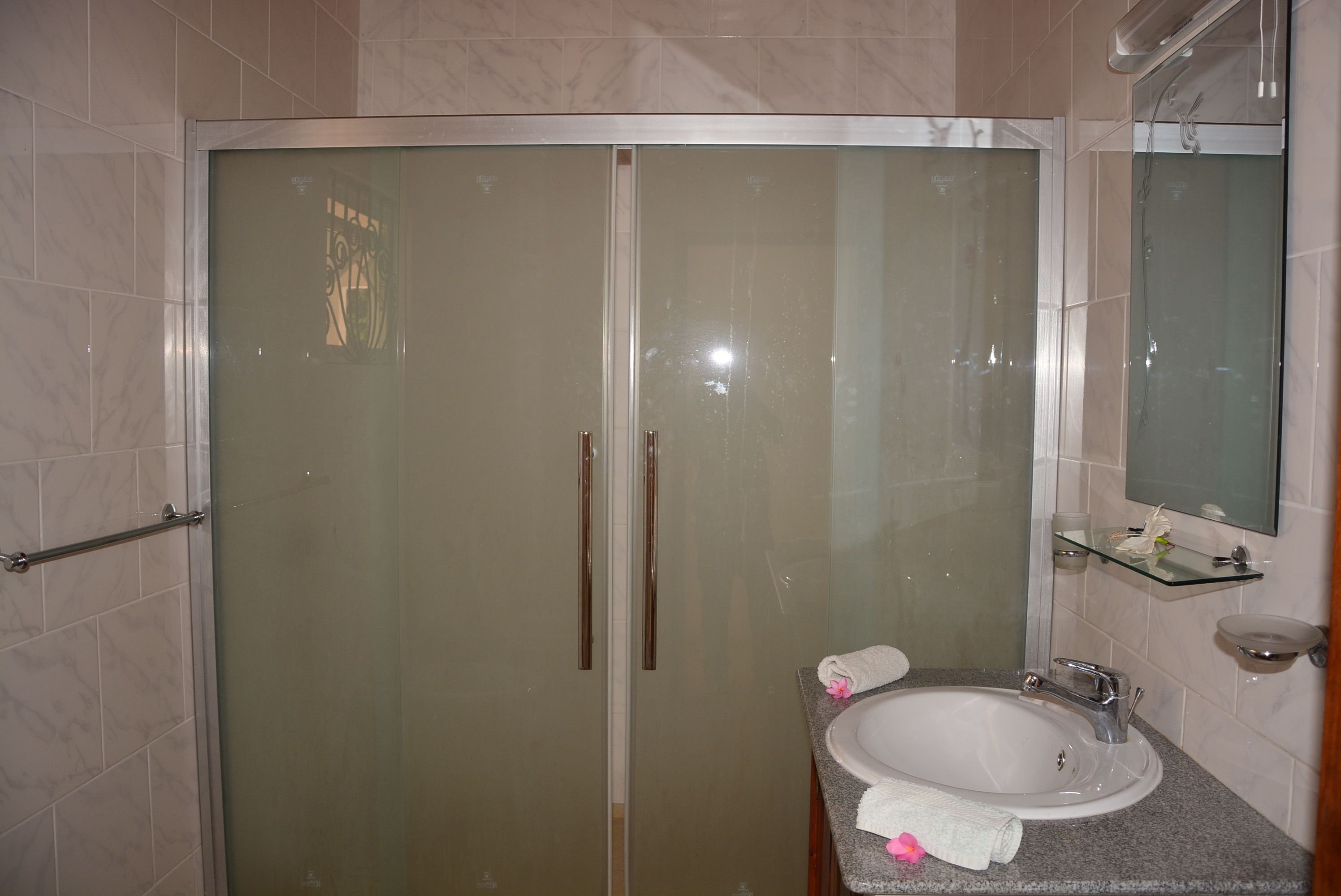 A bathroom with a glass-enclosed shower, a sink with a marble countertop, and a glass shelf with toiletries.