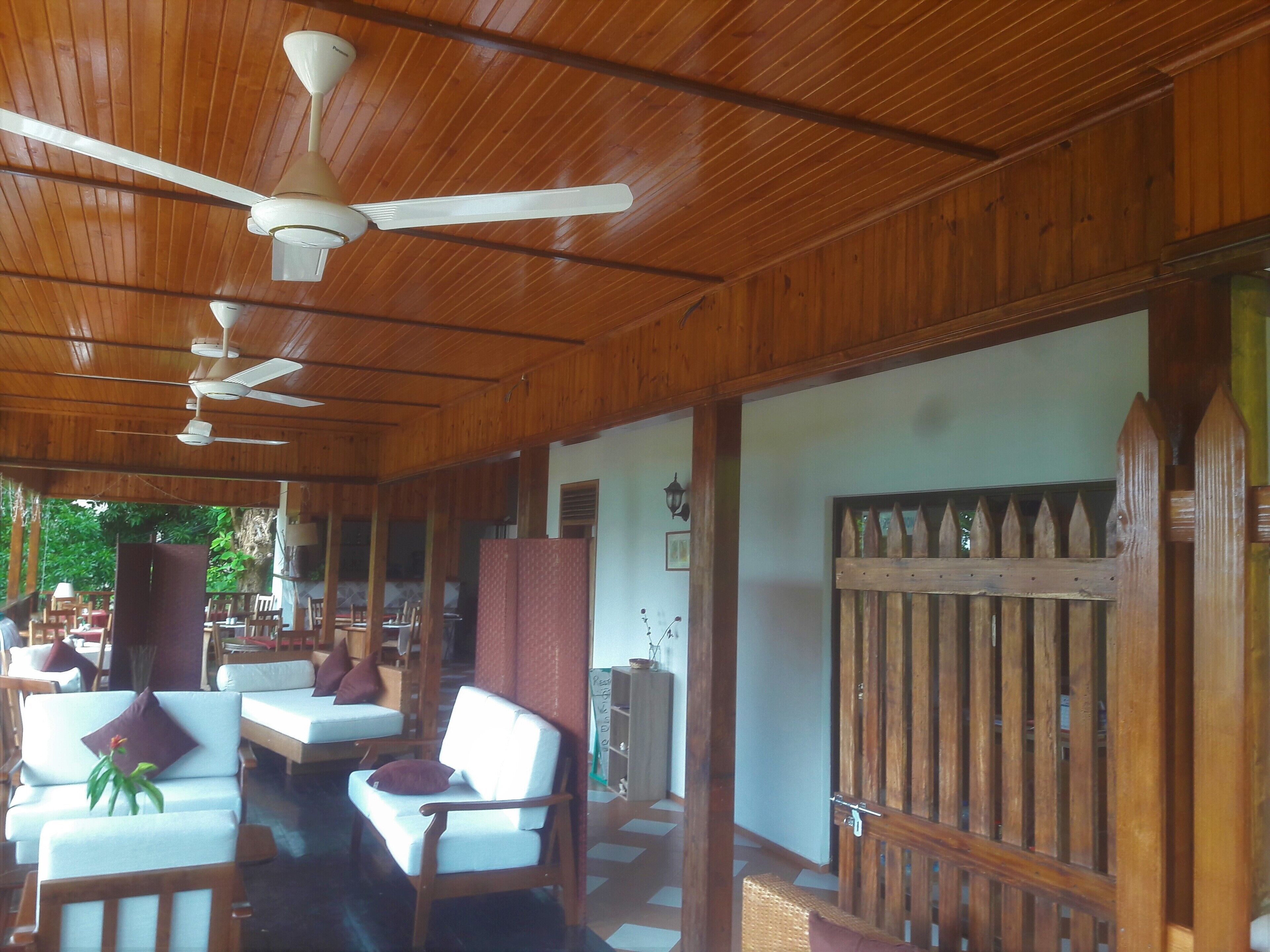 Area salotto esterna coperta con mobili in legno e ventilatori a soffitto.