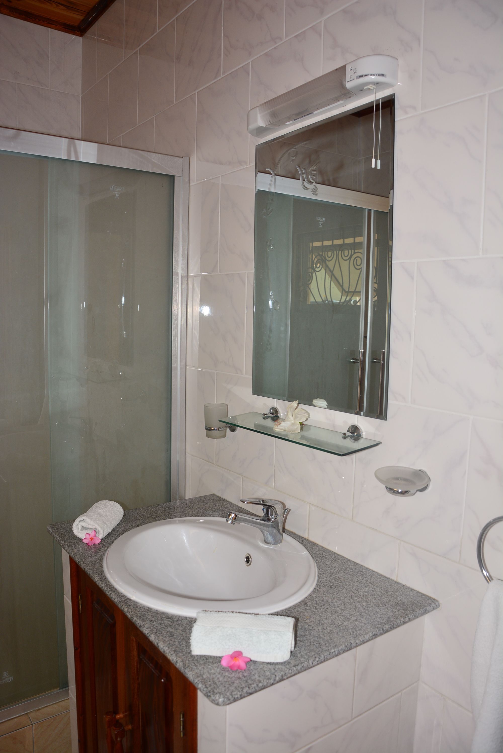 Un baño con cabina de ducha de vidrio, un lavabo blanco con encimera de mármol y un espejo sobre el lavabo.