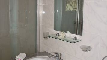 Un baño con cabina de ducha de vidrio, un lavabo blanco con encimera de mármol y un espejo sobre el lavabo.