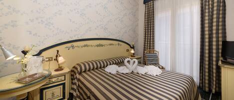 A hotel room with a bed, a bedside table with a lamp, a TV, and a window with curtains.