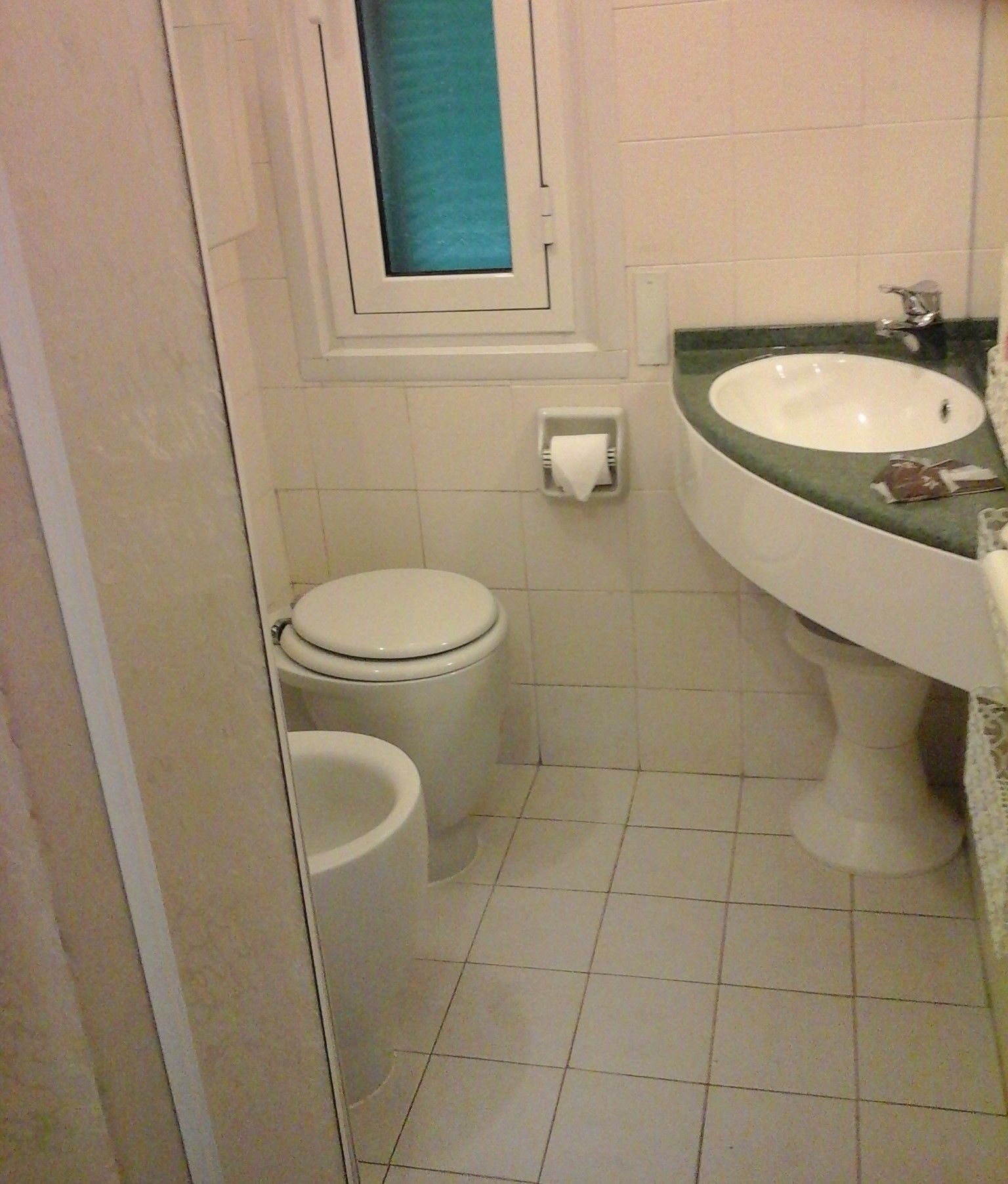 Une petite salle de bain avec des toilettes, un lavabo et une fenêtre.