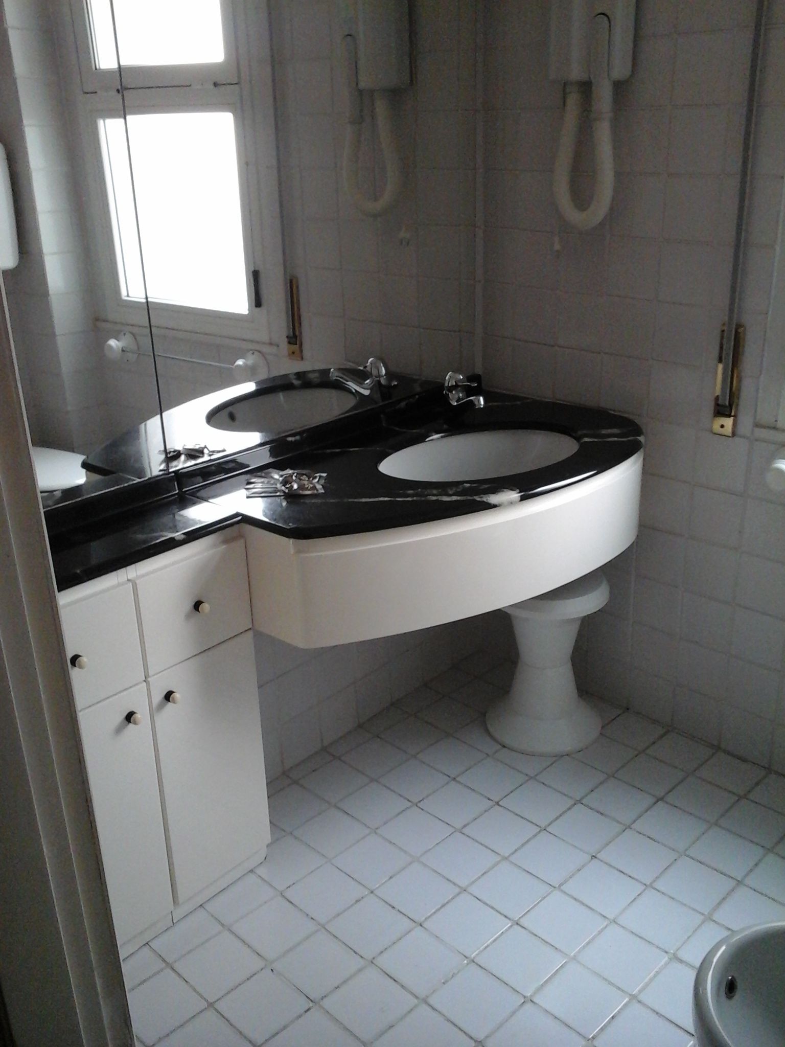 A bathroom with a double sink, white tiles, and a toilet.