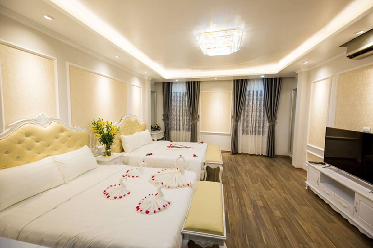 A hotel room with three beds, a TV, and a chandelier.