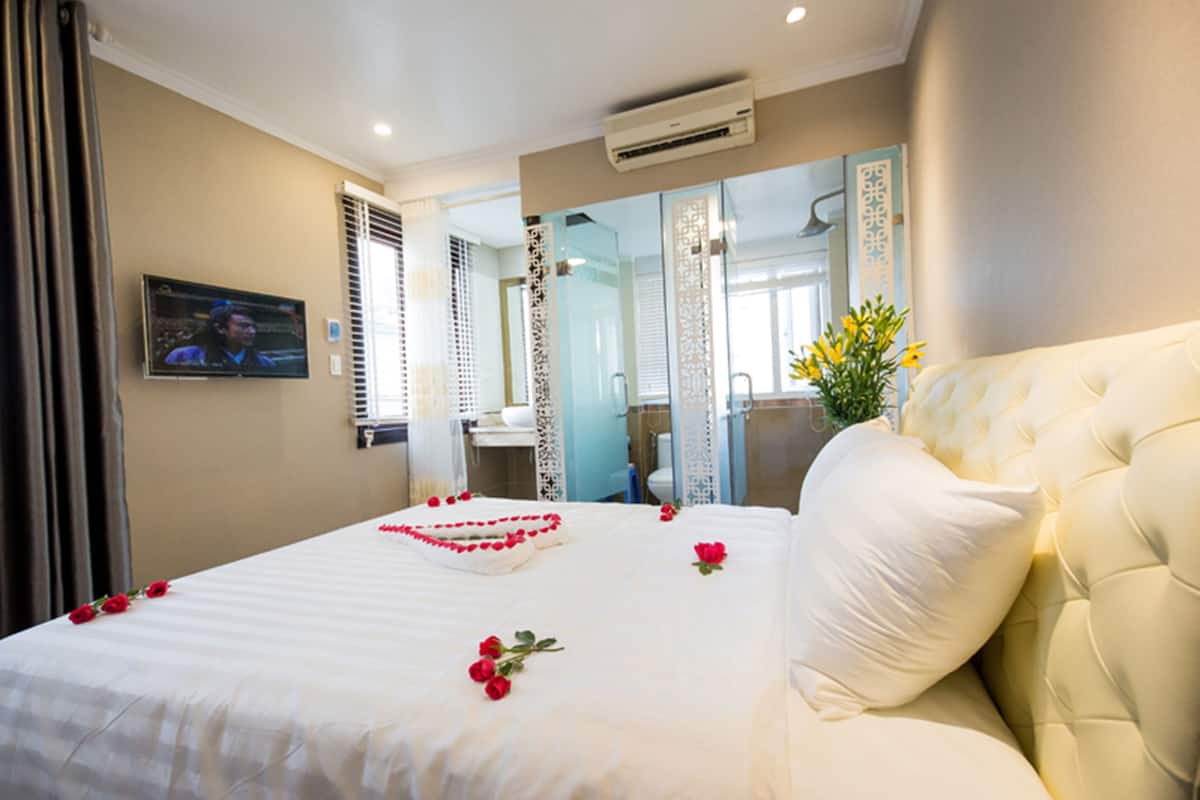 A hotel room with a large bed, a television, and a bathroom visible through a glass partition.