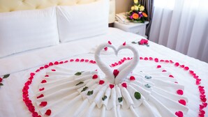 Una cama impecable con una toalla dispuesta en forma de corazón y pétalos de rosa.