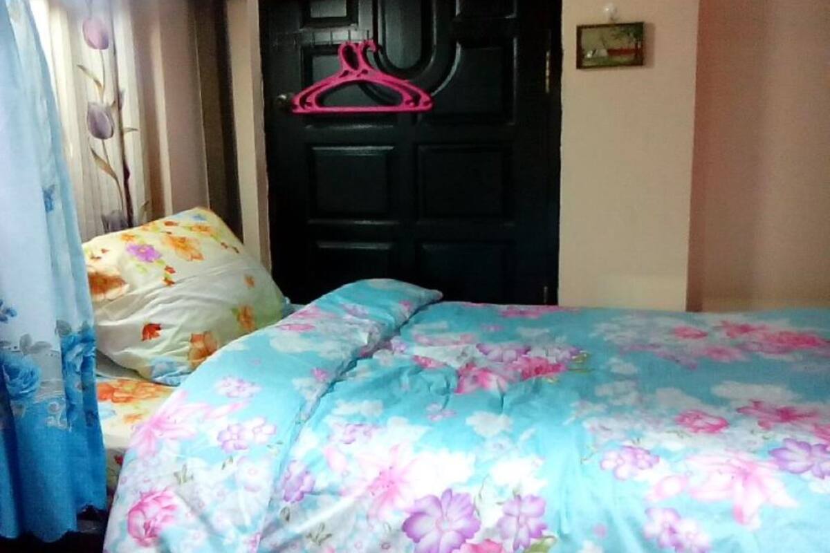 A bedroom with a bed covered in floral bedding, a black door with a pink hanger, and a window with curtains.