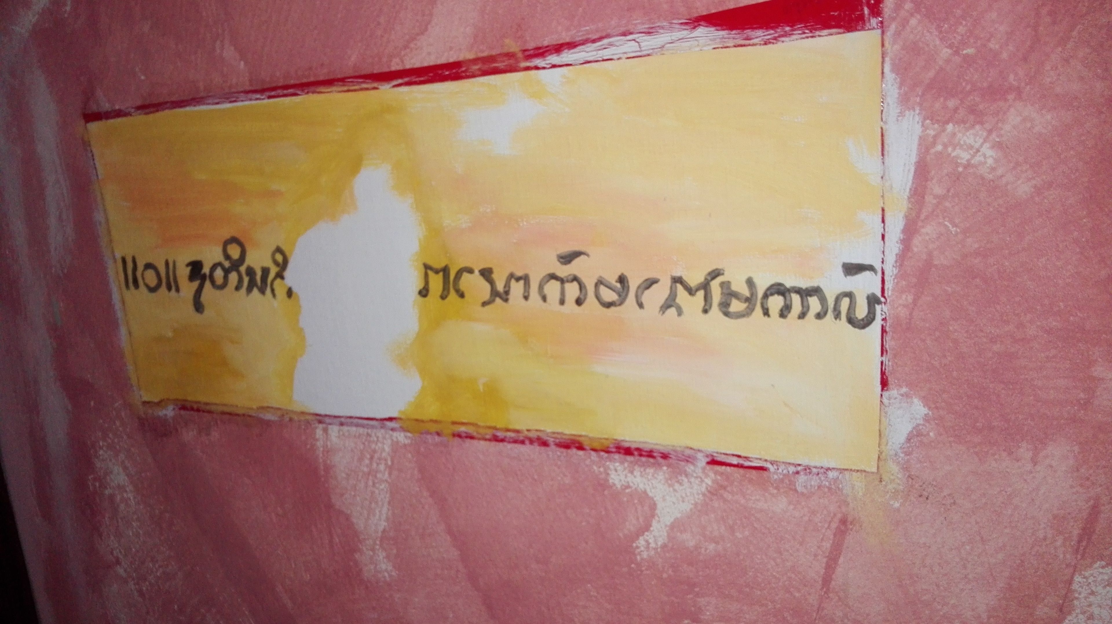 A wall with a yellow and red sign with text in a non-Latin script.