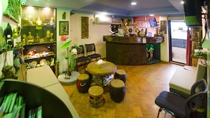 A room with a reception desk, several chairs, a table with a flower arrangement, and shelves with various items. - Shannkalay Hostel (Yangon)