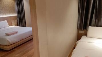 Habitación de hotel con dos camas, piso de madera y cortinas oscuras.