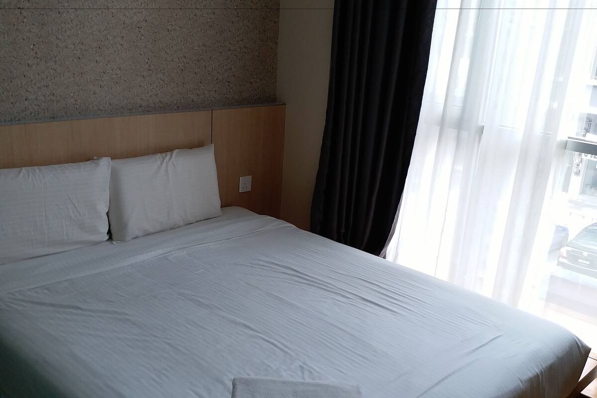 A hotel room with a large bed, a headboard, a wall with a textured pattern, and a window with curtains.