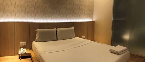 A neatly made bed with a headboard, a bedside table with a phone, and a wall with a textured pattern.