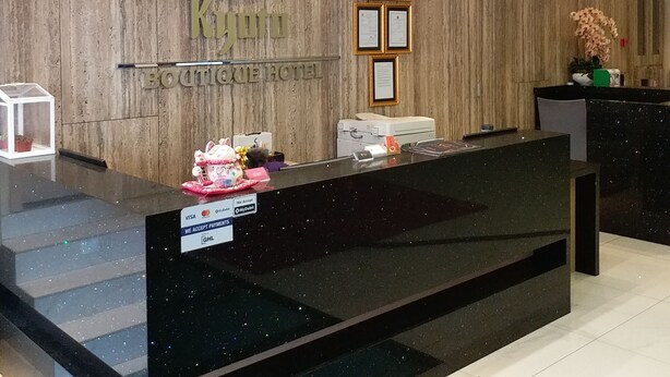 A hotel reception desk with a wooden backdrop, framed certificates, and a clock.