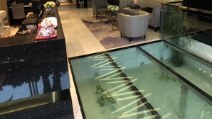 A modern lobby with a reception desk, seating area, and a glass-bottomed water feature.
