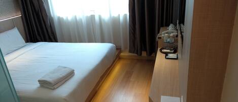A hotel room with a bed, a bedside table with a phone and water bottles, and a window with curtains.
