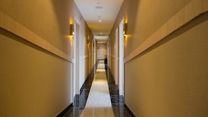A long, narrow hallway with a marble floor and wall-mounted lighting.
