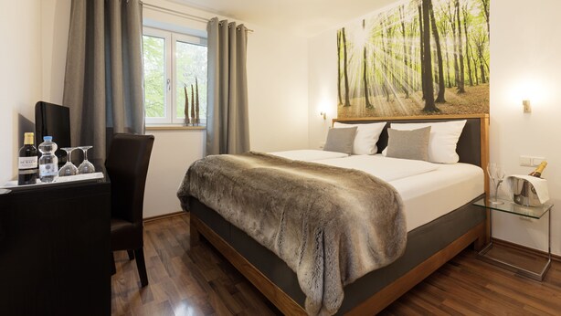 Une chambre avec un grand lit, un bureau avec un ordinateur, une chaise, une fenêtre avec des rideaux et une décoration murale sur le thème de la forêt.