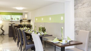 Un espace de repas moderne avec une longue table dressée pour accueillir plusieurs personnes, une cuisine en arrière-plan et un mur d’accent en pierre.
