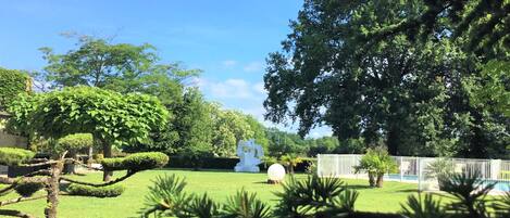 Un jardín bien cuidado con varios árboles, una escultura esférica blanca y un área cercada.