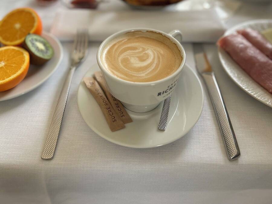 A breakfast setting with a cup of coffee, orange slices, kiwi, a plate of croissants, and a glass of orange juice.