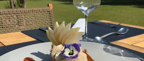 A dessert on a white plate with a glass of white wine on a table outdoors.