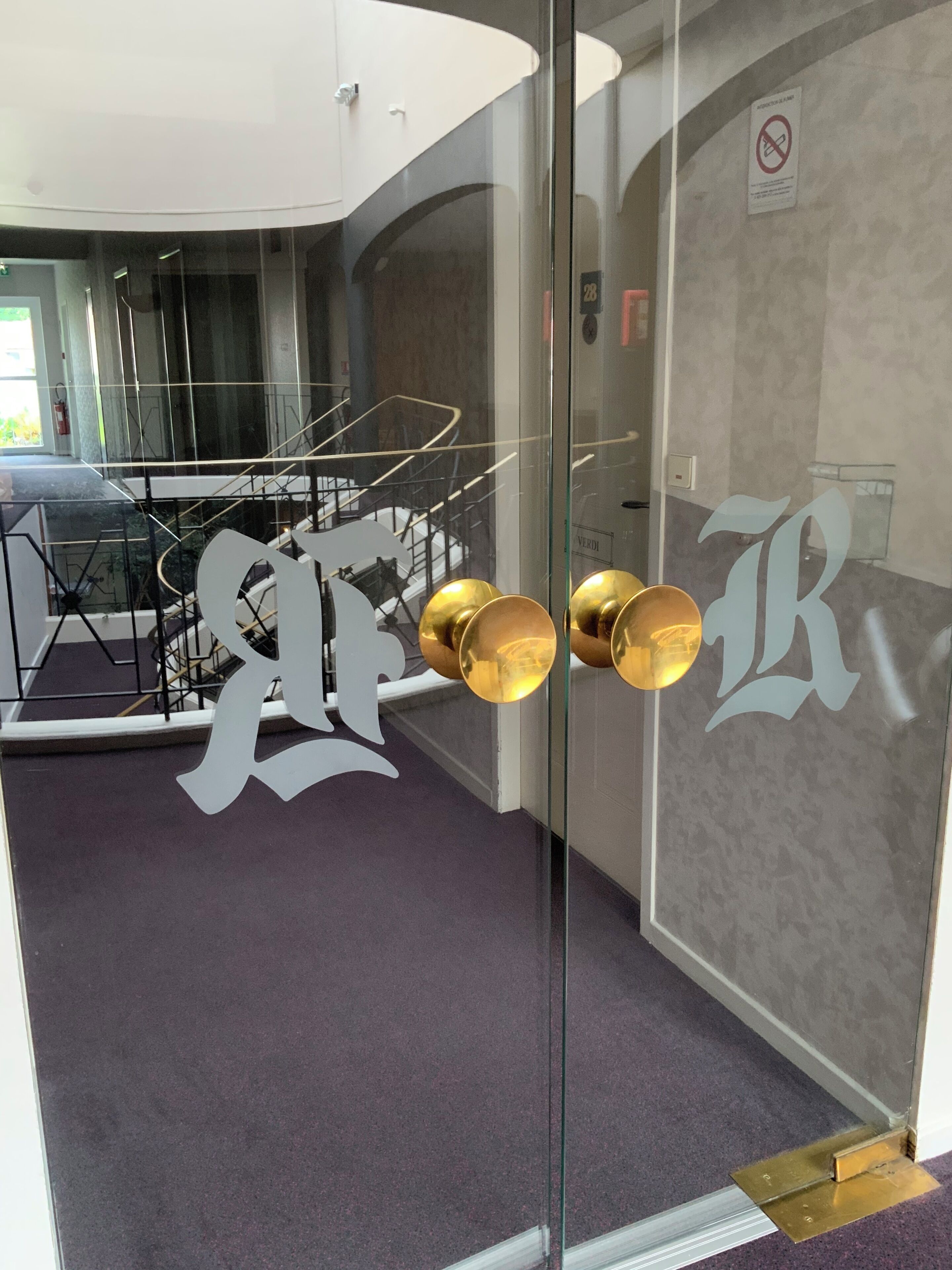 A modern interior with a glass door featuring large decorative letters and a reflection of a staircase.