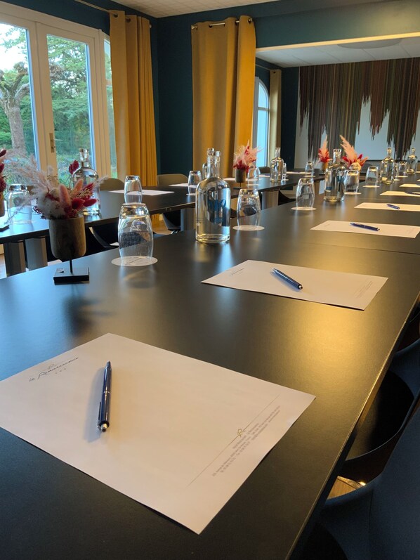Un salón de conferencias con una larga mesa dispuesta para una reunión, que incluye vasos, documentos y bolígrafos.