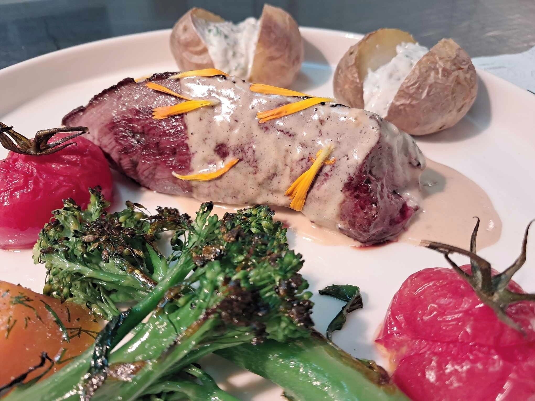 Un plato con un rollito de carne, patatas asadas y verduras.