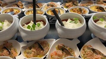 Una mesa de buffet con diversos platos en cuencos de cerámica blanca, algunos con adornos y otros con mariscos.