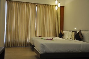 Quarto de hotel com duas camas, cortinas bege e piso de madeira.