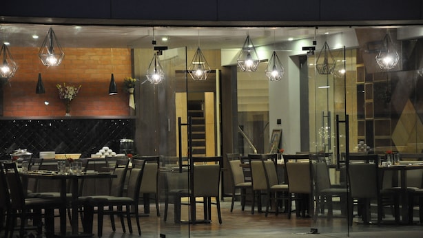 A modern dining area with glass partitions, contemporary lighting fixtures, and a brick accent wall. - Pride Biznotel Alkapuri (Savli)
