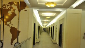 A long, narrow hotel corridor with a central walkway, flanked by doors on both sides. - Pride Biznotel Alkapuri (Savli)