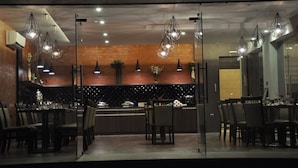 A modern restaurant with a brick wall, glass partition, and hanging pendant lights. - Pride Biznotel Alkapuri (Savli)