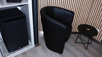 A compact room with a black refrigerator, a black chair, and a small round table.
