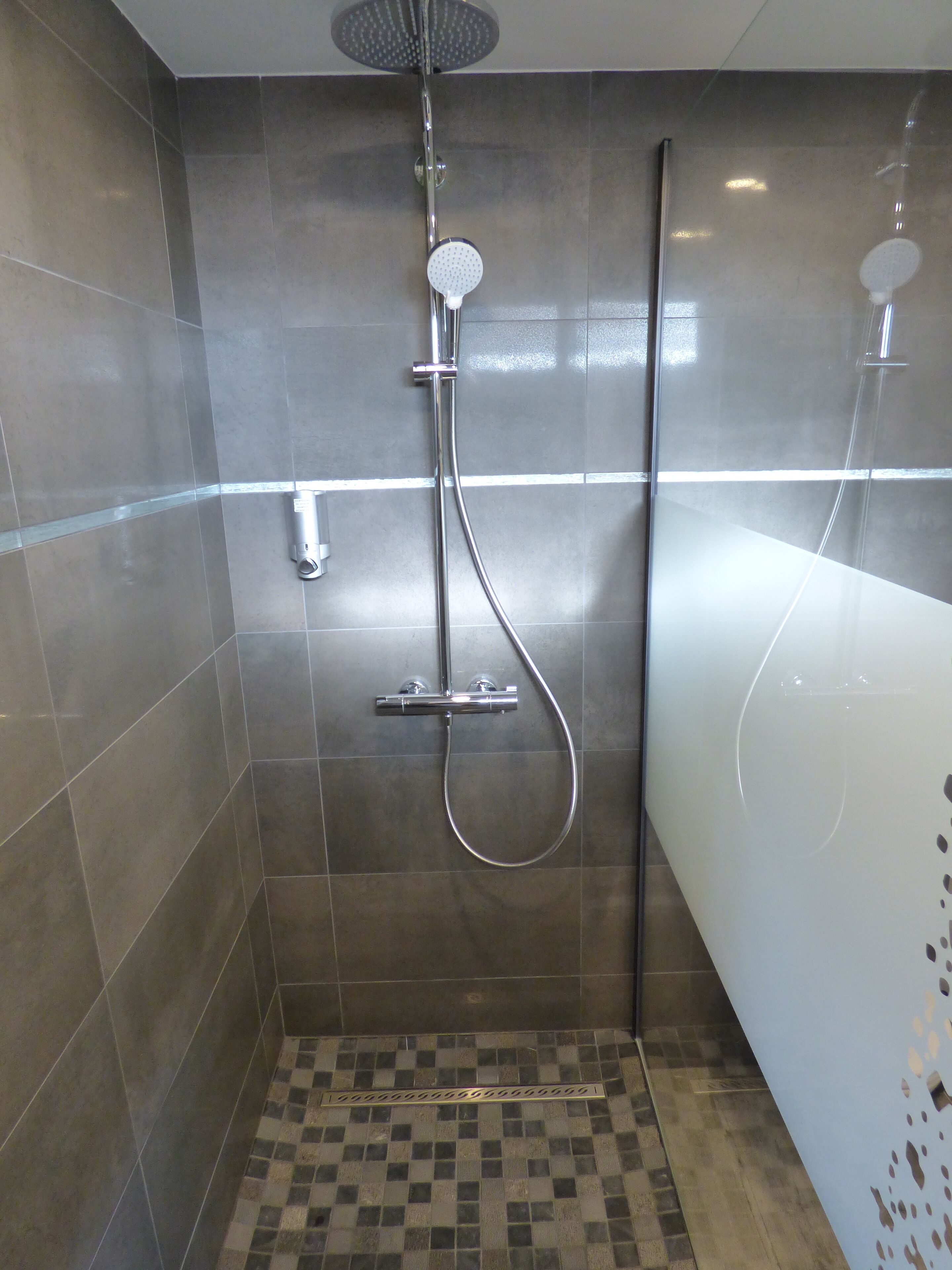 Un área de ducha con cabezal de ducha de mano, cabezal de ducha empotrado y una bañera.
