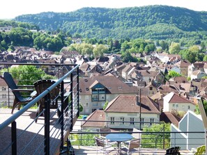 A residential area with traditional European architecture, a balcony with outdoor furniture, and a view of a hill with dense greenery. - La Colline aux Yeux Doubs (Baume-les-Dames)