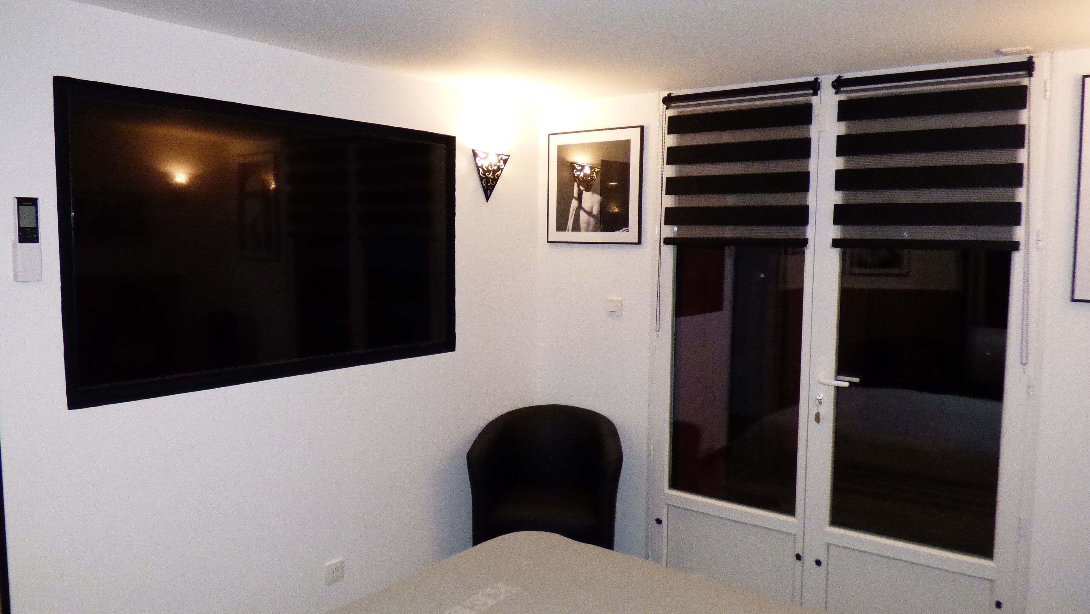 A room with a large flat-screen TV mounted on the wall, a framed picture above a door, and a sliding glass door with blinds.