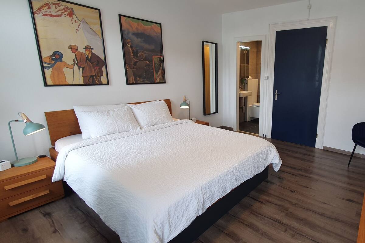 Quarto com cama, mesas de cabeceira, escrivaninha, cadeira e obras de arte na parede.