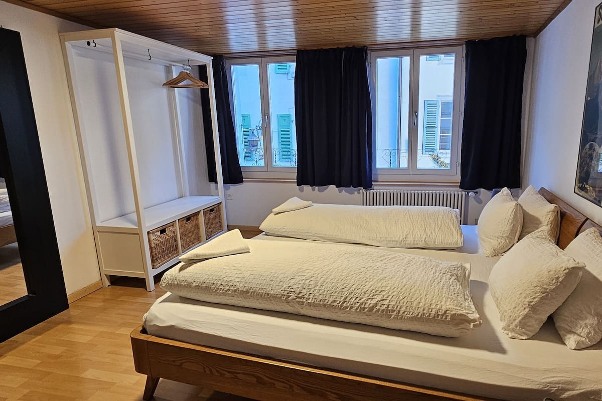 Quarto com cama de madeira, guarda-roupa, espelho e janela com cortinas.