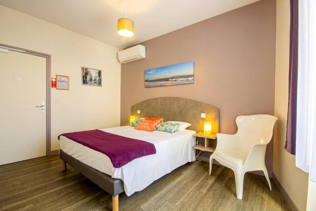 A bedroom with a bed, bedside lamps, a chair, a painting, and a door.