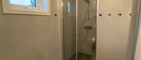 A glass-enclosed shower with a handheld showerhead and a wall-mounted faucet.