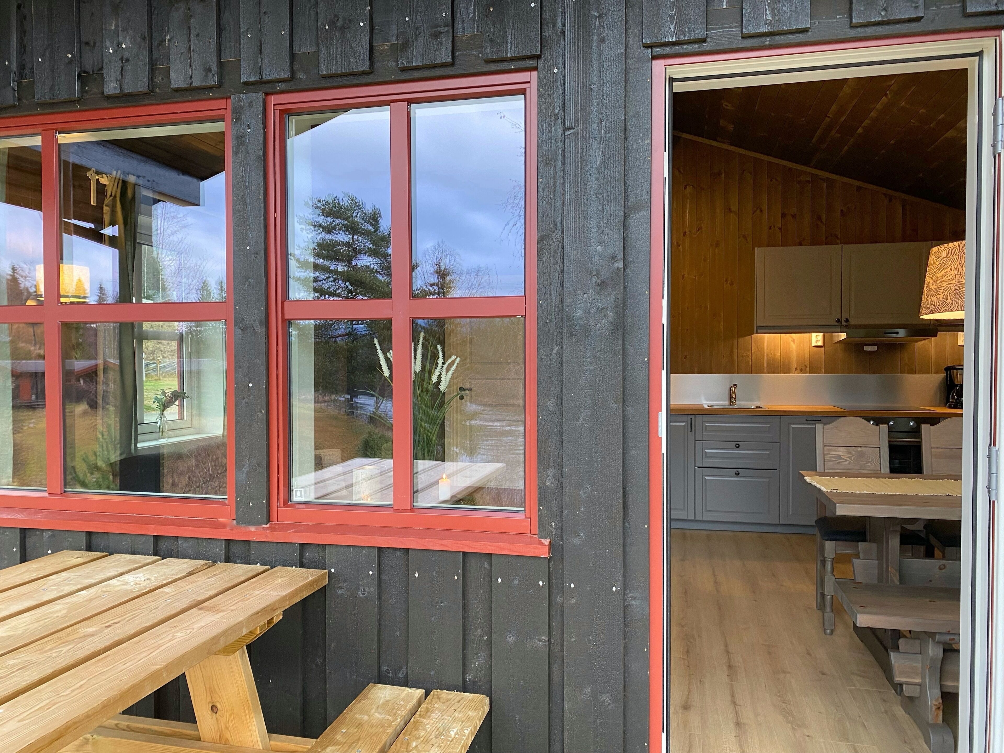 Una cabaña rústica con fachada de madera, una zona de comedor con mesa y bancos de madera, y una cocina con armarios y encimera de madera.